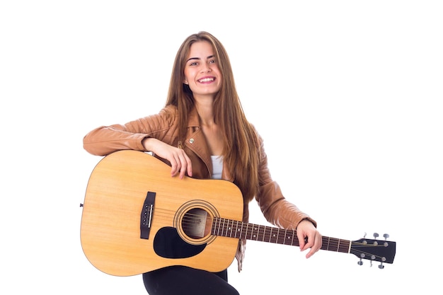 Hübsche junge Frau in brauner Jacke und schwarzer Hose, die im Studio Gitarre spielt