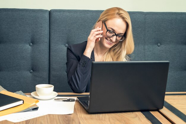 Hübsche junge Frau in Brille telefoniert im Büro mit einem Kunden.