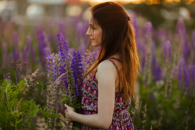 Hübsche junge Frau in einem Feld bei Sonnenuntergang. Blumen halten