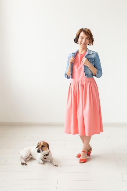 Hübsche junge Frau in einem langen eleganten Kleid und in einem Jeanshemd, das auf einer weißen Wand aufwirft