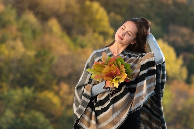 Hübsche junge Frau in einem Poncho mit Herbstlaub in den Händen. Mädchen berührte das Haar. Porträt.