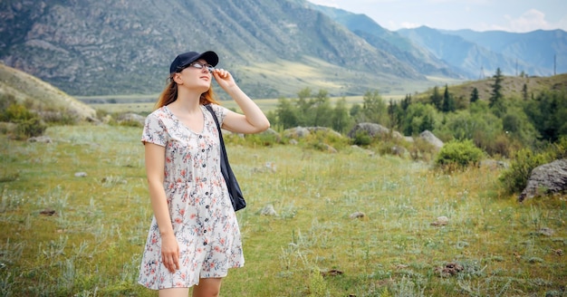 Hübsche junge Frau in Mütze und kurzem Kleid bewundert die schöne Aussicht in den Bergen Wandern im Freien Aktivitäten Sommerferien der Studentin