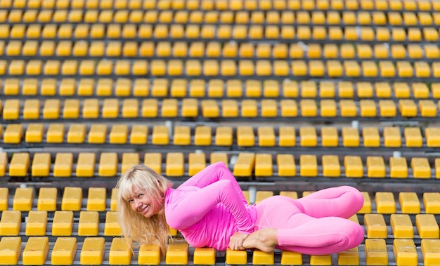 Hübsche junge Frau in rosa Sportkleidung, die am sonnigen Tag auf gelbem Hintergrund Yoga-Asanas im Park macht