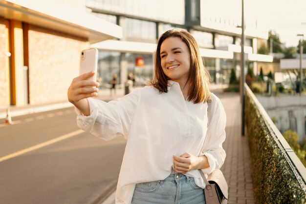 Hübsche junge Frau macht ein Selfie mit ihrem Telefon, während sie spazieren geht