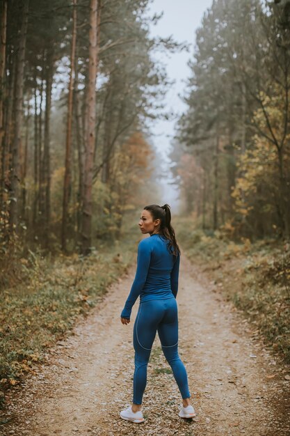 Hübsche junge Frau macht im Herbst eine Pause beim Outdoor-Training auf dem Waldweg