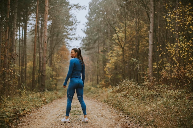 Hübsche junge Frau macht im Herbst eine Pause beim Outdoor-Training auf dem Waldweg