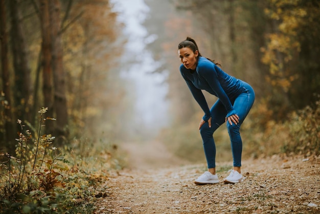 Hübsche junge Frau macht im Herbst eine Pause beim Outdoor-Training auf dem Waldweg