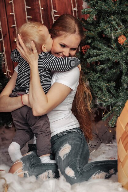 Hübsche junge Frau mit einem einjährigen Kind, das am Weihnachtsbaum spielt