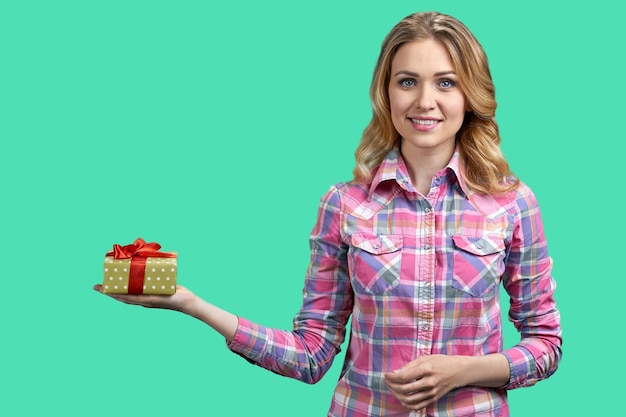 Hübsche junge Frau mit Geschenkbox und Blick in die Kamera auf grünem Hintergrund