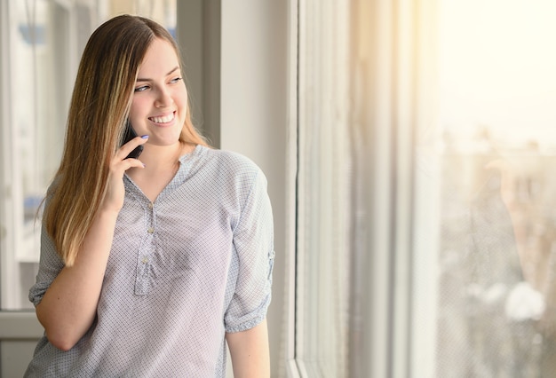 Hübsche junge Frau mit Handy am Fenster