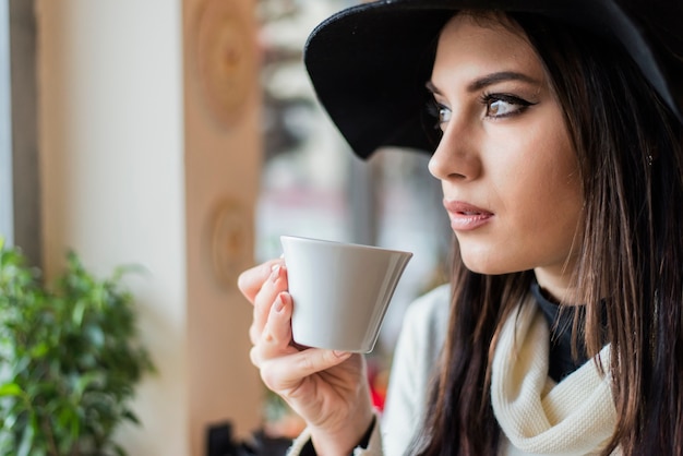 Hübsche junge Frau mit Hut, der Kaffee trinkt