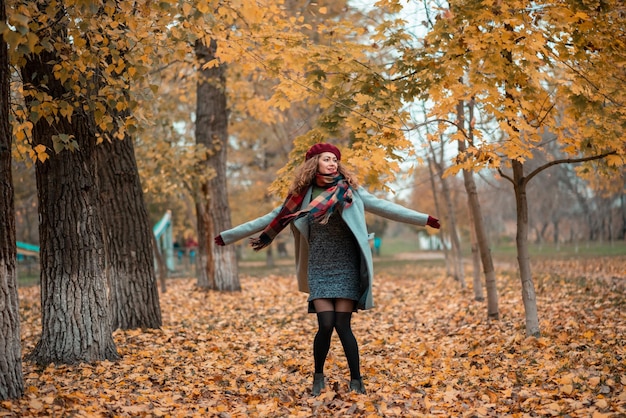 Hübsche junge Frau mit langen lockigen Haaren im Herbstpark auf dem Hintergrund gelber Blätter, die fröhlich mit schönen Herbstfarben tanzen