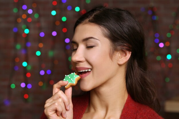 Hübsche junge Frau mit leckerem Weihnachtsplätzchen gegen defokussierte Lichter