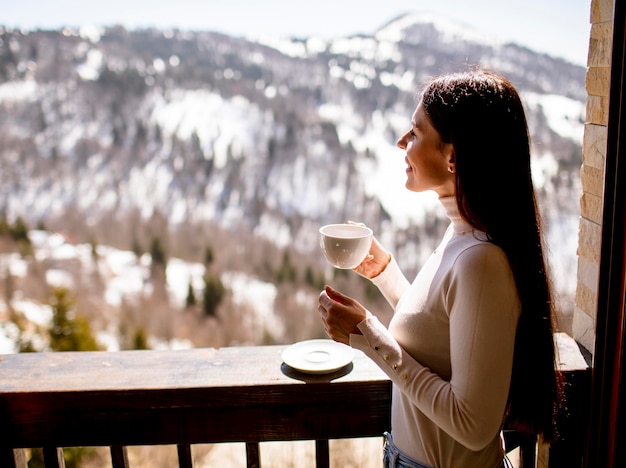 Hübsche junge Frau mit Tasse heißen Tee im Winterfenster