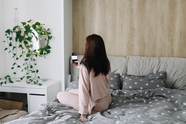 Hübsche junge Frau sitzt im Bett und macht Selfie