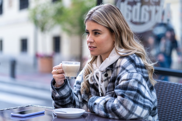 Hübsche junge Frau trinkt Kaffee auf der Terrasse einer Bar