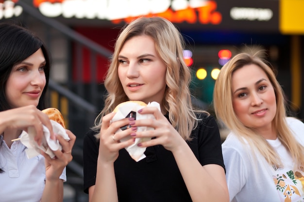 Hübsche junge Frauen essen Hamburger im Freien auf der Straße.