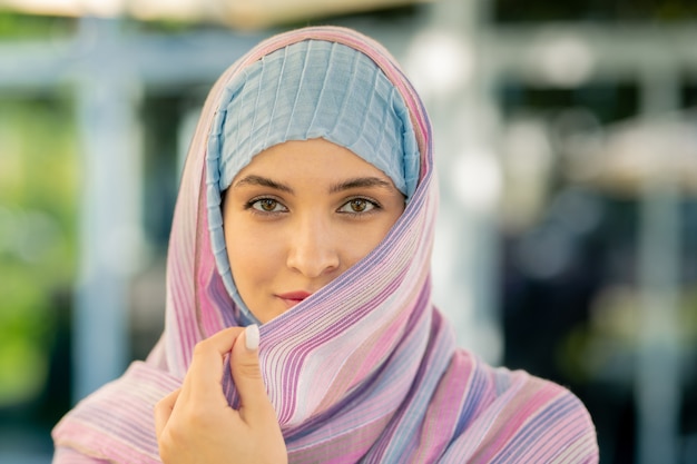 Hübsche junge muslimische Frau im traditionellen Hijab, der Sie beim Verweilen im Freien betrachtet
