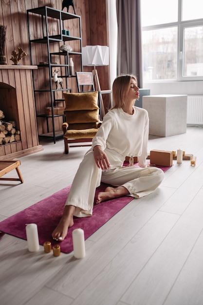 Foto hübsche junge ruhige frau meditiert entspannendes sitzen auf natürlicher matte in gemütlichem interieur am wochenende. wellness der frau