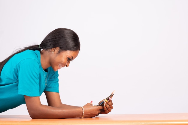 Hübsche junge schwarze Frau, die auf einem Schreibtisch stillsteht und ihr Telefon benutzt