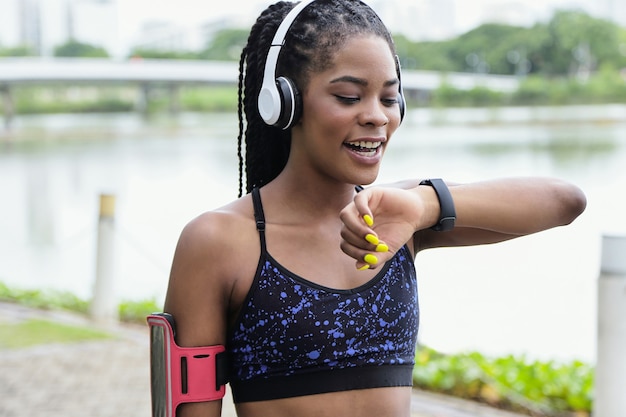 Hübsche junge Sportlerin, die Sprachnachricht für Freund über Anwendung auf Smartwatch beim Training im Park aufzeichnet