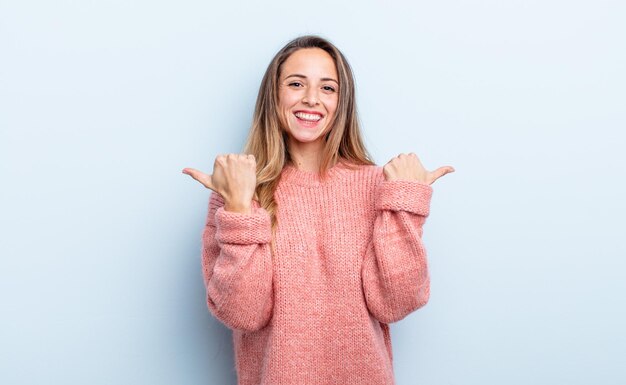 Hübsche kaukasische Frau, die freudig lächelt und glücklich aussieht, sich sorglos und positiv mit beiden Daumen nach oben fühlt