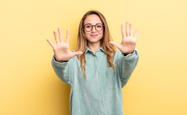 Hübsche kaukasische Frau, die lächelt und freundlich aussieht, die Nummer zehn oder zehn mit der Hand nach vorne zeigt und herunterzählt