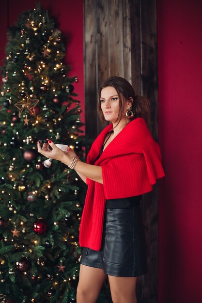 Hübsche kaukasische Frau mit dunklem Haar im schwarzen Kleid nahe dem großen Weihnachtsbaum