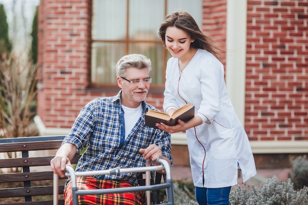 Foto hübsche krankenschwester, die ein buch für alten mann nahe hispital liest