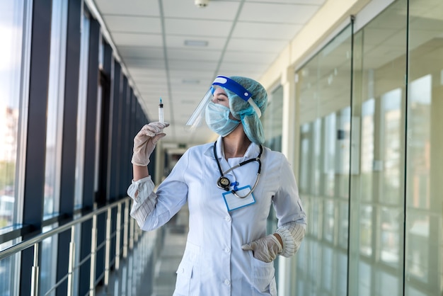 Hübsche Krankenschwester in Uniform und Gesichtsschutz, die Spritze hält und Impfung in der Klinik wartet