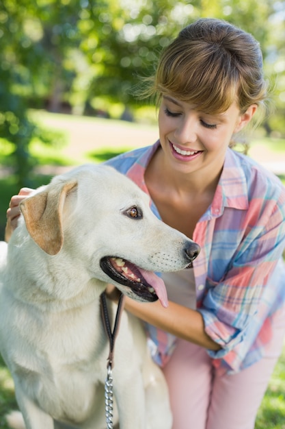 Hübsche lächelnde blonde Aufstellung mit ihrem Labrador im Park