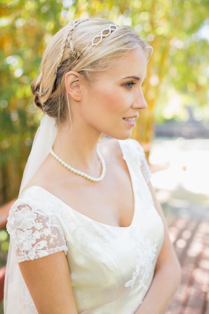 Hübsche lächelnde blonde Braut, die auf einer Brücke steht