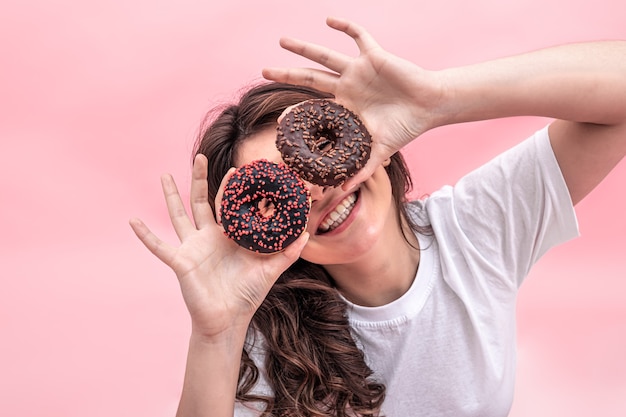 Hübsche lächelnde Frau, die Donuts in ihren Händen auf einem rosa Hintergrund hält