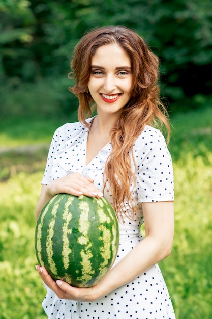 Hübsche lächelnde Frau, die eine Wassermelone hält