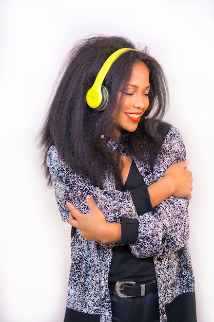 hübsche lächelnde hispanische Frau, die Musik mit Kopfhörern auf weißer Wand genießt