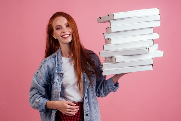 Hübsche, lange, rothaarige Ingwerfrau, die viele Kisten mit Fast-Food-Snack hält, isolierte rosafarbene Hintergrundstudioaufnahme. lieferung für home-party-konzept.