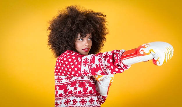 hübsche lateinamerikanische hispanische Frau zu Weihnachten, auf der Hut mit Boxhandschuhen. Gelber Hintergrund