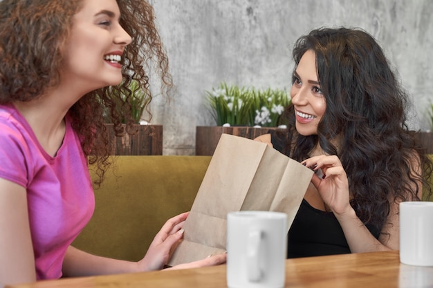 Hübsche lockige Frau, die Freundin im Café Geschenk macht