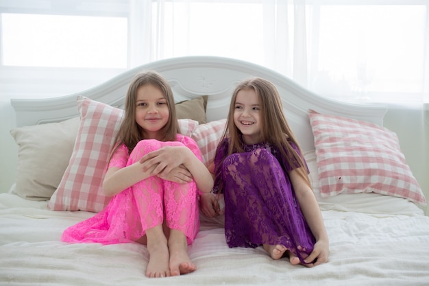 Hübsche Mädchen in rosa und lila Kleidern sitzen auf dem Bett