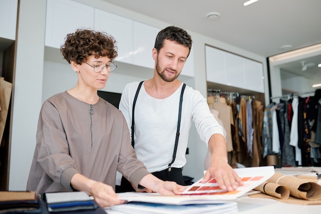 Hübsche Modedesignerin und ihre Kollegin schauen sich das Farbmuster an, während sie darüber diskutieren