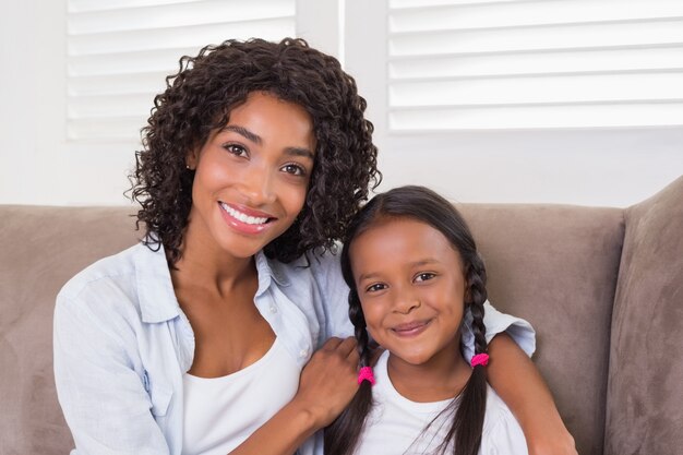 Hübsche Mutter, die auf der Couch mit ihrer Tochter lächelt an der Kamera sitzt