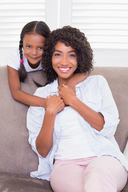 Hübsche Mutter, die auf der Couch mit ihrer Tochter lächelt an der Kamera sitzt