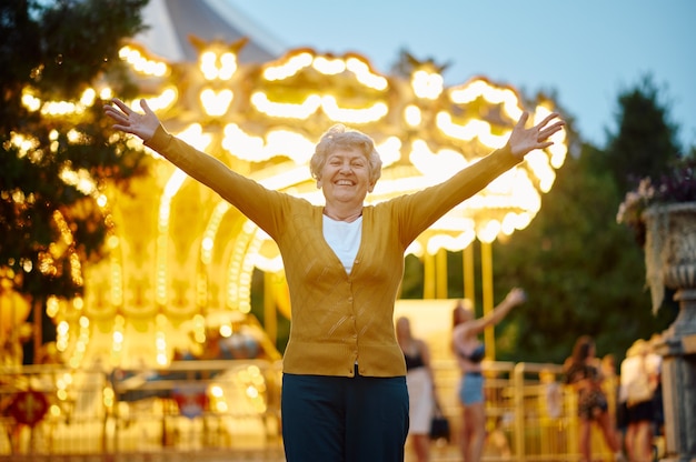 Hübsche Oma posiert im Sommer-Vergnügungspark, helle Beleuchtung im Hintergrund, zurück in die Kindheit. Lebensstil der älteren Menschen. Lustige Großmutter, die Spaß im Freien hat, alte weibliche Person auf Natur