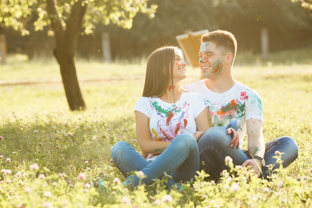 Hübsche Paare, die draußen am Gras sitzen. Schönes Mädchen und gutaussehender Mann, die einander betrachtet und am Freilicht trägt colorized T-Shirts lächelt