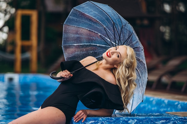 Hübsche Pin-up-Blondine im schwarzen Vintage-Badeanzug, die sich im Pool entspannt