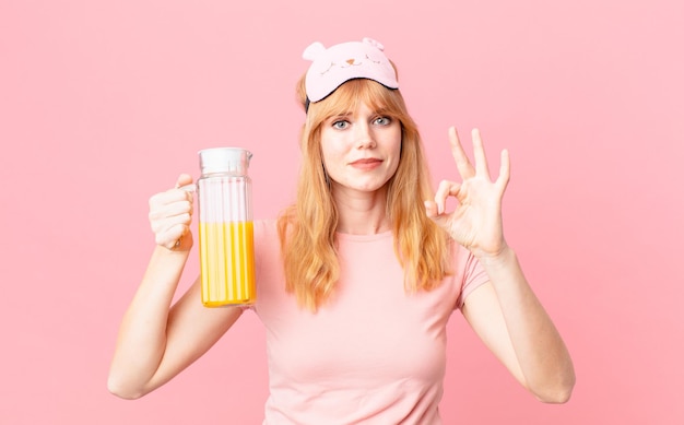 Foto hübsche rote hauptfrau, die pyjamas trägt und einen orangensaft hält. gesundes frühstückskonzept