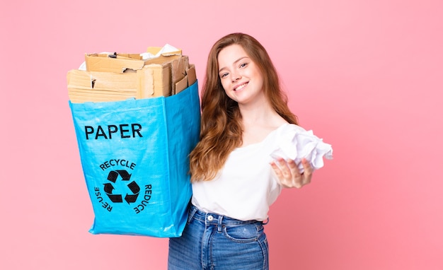 Hübsche rothaarige Frau, die eine Recyclingpapiertüte hält