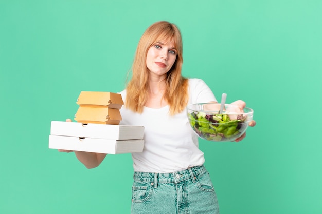 Hübsche rothaarige Frau mit Fast-Food-Boxen und einem Salat