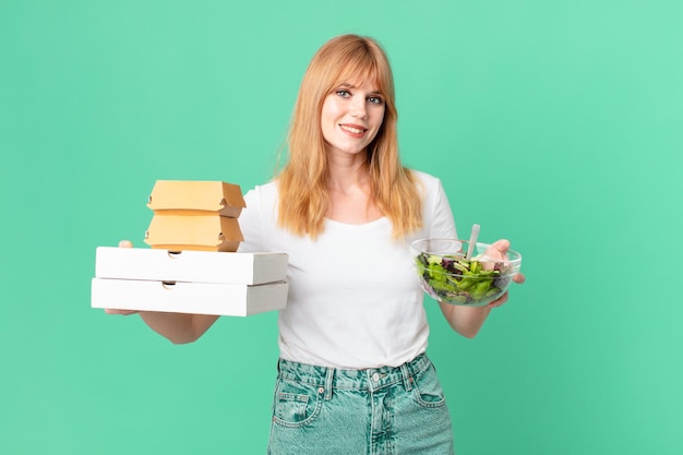 Hübsche rothaarige Frau mit Fastfood-Boxen und einem Salat