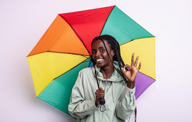 Hübsche schwarze Frau, die sich glücklich fühlt und Zustimmung mit okayer Geste zeigt. Regenschirmkonzept